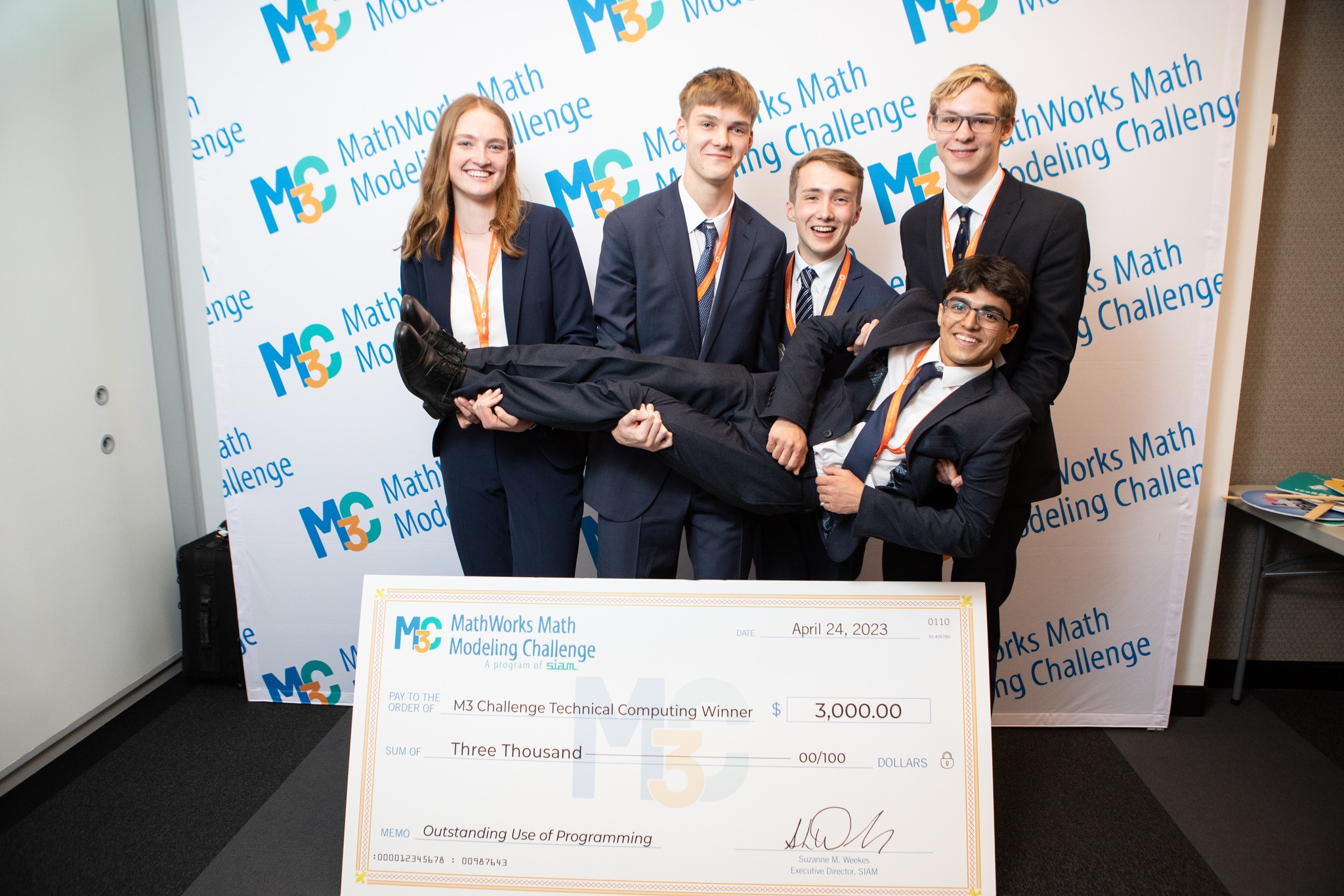 five students posing with a big check indicating they are the M3 Challenge Technical Computing Awardees; four of the students are lifting the fifth student