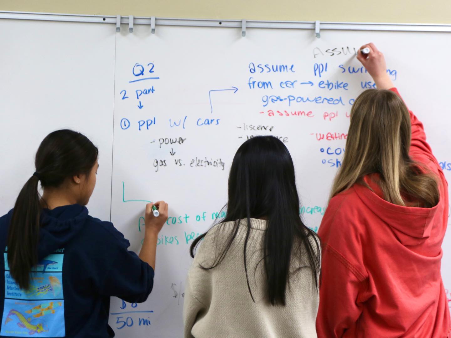 Three students writing on a whiteboard.