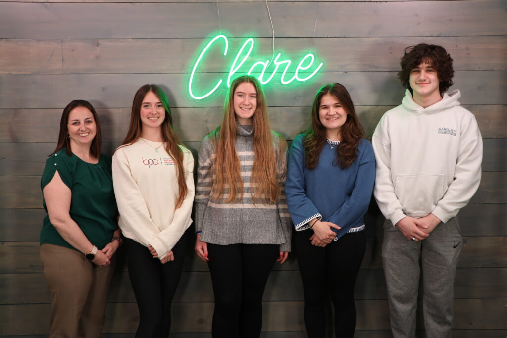1 teacher and 4 students pose by wall from Clare High School