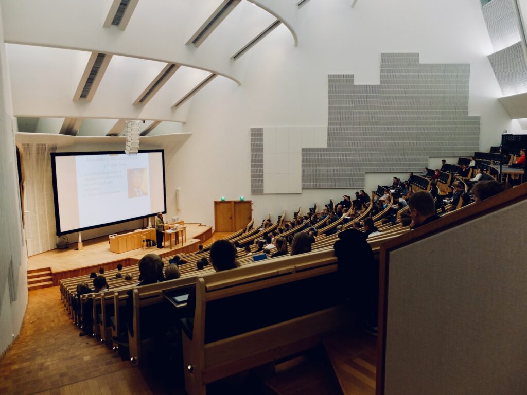 Students sitting in a lecture hall looking at someone presenting on stage. 