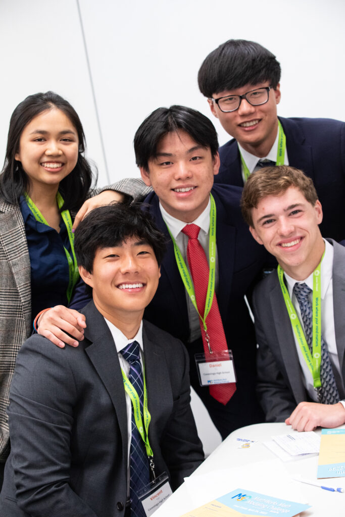 Students at one of the M3 Challenge final events grouped together at a table.