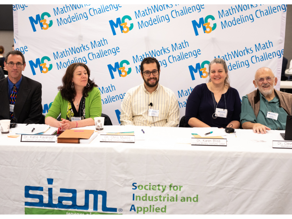 Three judges sitting at a table with a SIAM tablecloth.