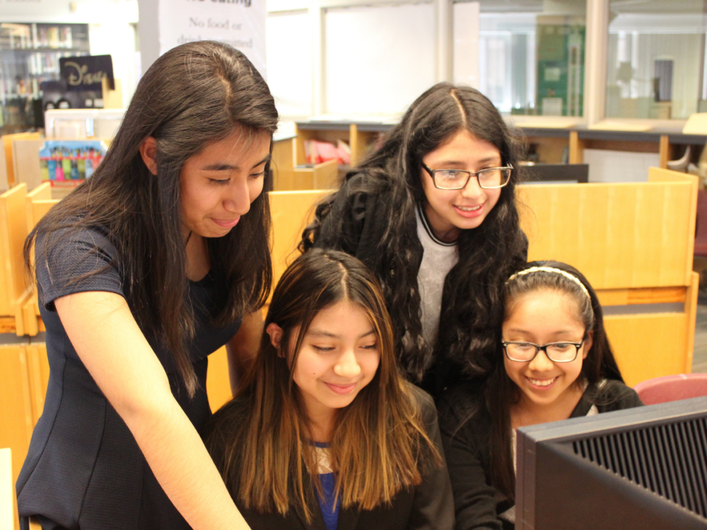 Four girls huddled around a computer.