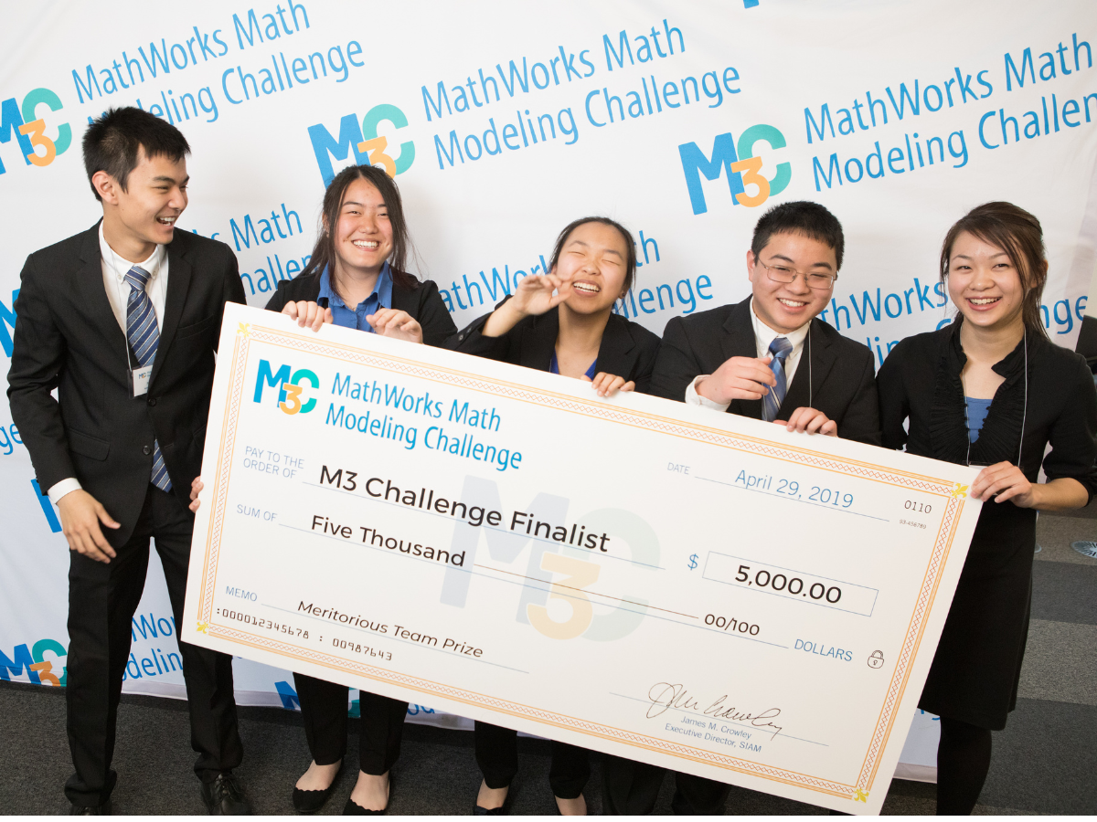 Five students smiling and laughing while holding a giant check after participating in the math competition.